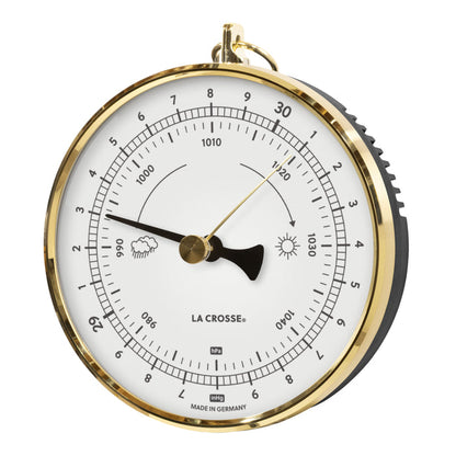 Left-facing image of the 138-1611W Analog Barometer - White featuring a brass case with a dome lens covering a white dial, brass reference marker, a black pressure indicator, black numbers, icons, and text. The barometer measures the atmospheric pressure in Hectopascals (hPa) and in Inches of Mercury (inHg) Made in Germany.