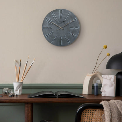 404-3028B Cormac 11 inch open face molded dark gray wall clock with numbers in relief and silver metal hour and minute hands hanging on a tan wall with green wainscotting over a dark wood desk and transitional decorative style accents