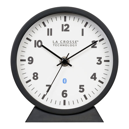 Head-on image of the 437-3816 Insta-Set Table/Wall Clock with Bluetooth® Technology featuring a white dial with bold black numerals, black metal hands, and a black frame with removable base for tabletop or wall hanging placement.