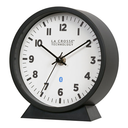 Left-facing image of the 437-3816 Insta-Set Table/Wall Clock with Bluetooth® Technology featuring a white dial with bold black numerals, black metal hands, and a black frame with removable base for tabletop or wall hanging placement.