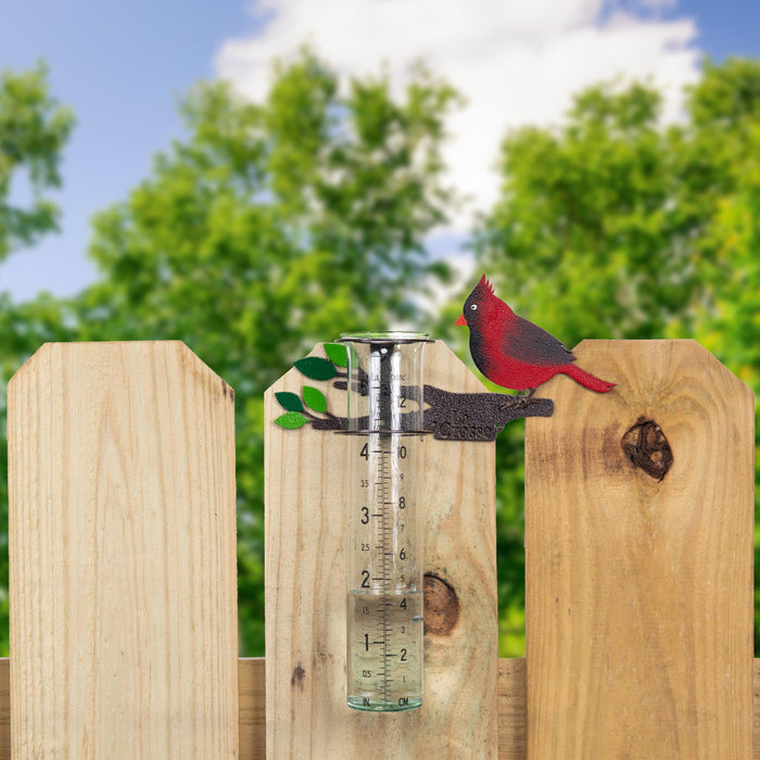 Lifestyle image of the 704-4612 Metal Cardinal rain gauge on a fence with a blue sky and trees in the background